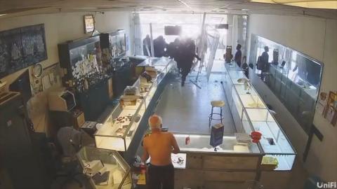 A man in a jewellery shop as masked people enter