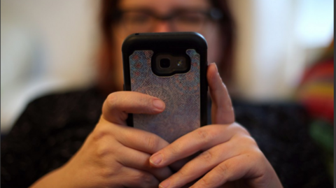 A blurred image of a woman wearing glasses using a mobile phone