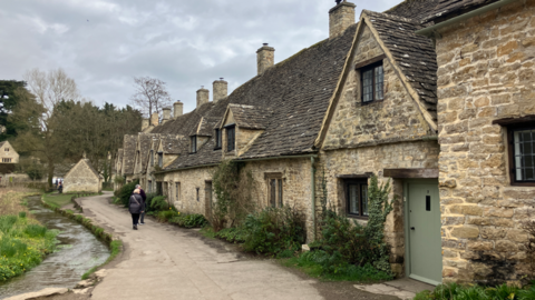 Typical chocolate box houses in the Cotswolds along a narrow village pathway and stream.