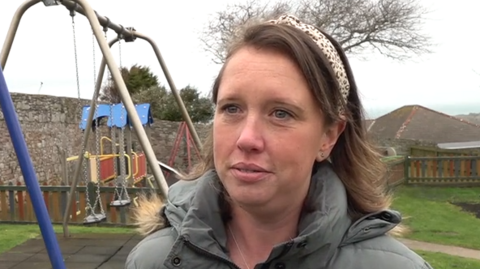 Beth Chapman, chairwoman of St Anne's School's Parent Teacher Association. She is stood in an empty playground. She is wearing a grey Parka coat and has a leopard print head band on.