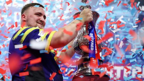 Luke Littler raises the Phil Taylor Trophy