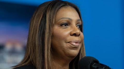 Letitia James with a blue background, holding a microphone