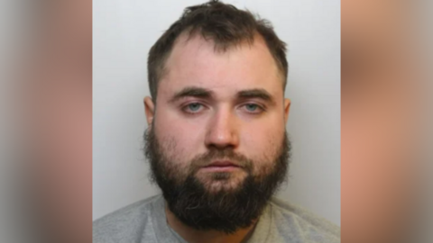 Victor Rotundu is looking at the camera in a police custody picture. He has a bushy, unkept beard.
