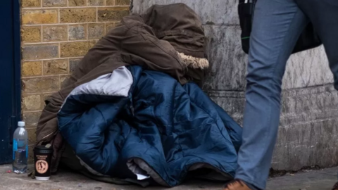 Homeless person with coat on and sleeping bag while someone walks past