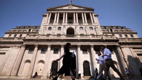 Slightly blurry pedestrians in smart clothing walk in front of the Bank of England building