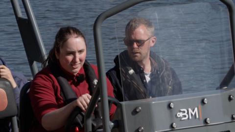 A young women next to an instructor at the wheel of a RIB speedboat. 