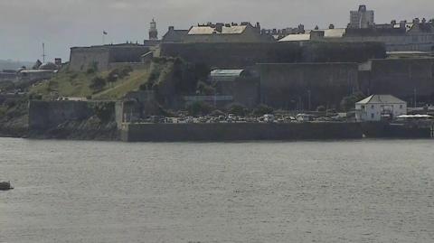 A CCTV picture of the harbour showing boats water and land in the background. The two swimmers in the water are barely visible. 