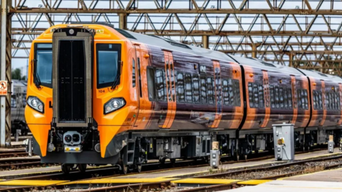 A West Midlands Railway train, with orange and purple livery, on tracks.