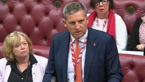 Lord James Timpson speaks in the House of Lords with red benches seen behind him.