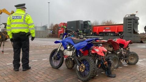 A police officer stood next to some off road bikes.