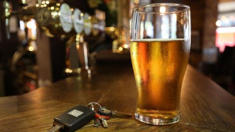 A picture of a pint of beer on a bar with keys beside it on the left. In the background is the bar and a window to the right 