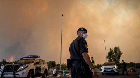 A Spanish Civil Guard officer wears a protective mask as smoke from a wildfire obscures the sky in Cenicientos, Madrid