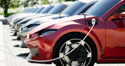 A row of cars parked at electric charging points. The nearest car is red.