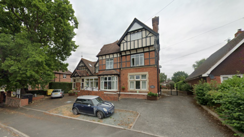 A three storey Edwardian house pictured with a blue Mini Cooper parked outside it. 