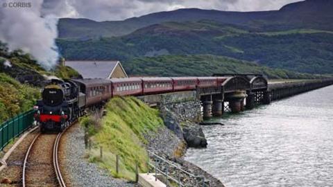 A steam locomotive crosses a bridge over water.