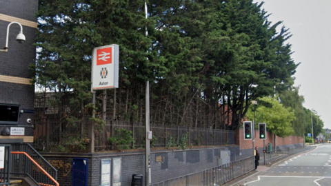 A sign showing Aston railway station by the side of a road