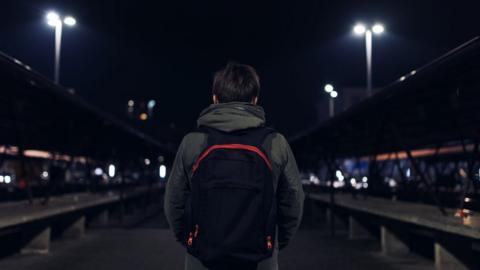 Rear view of young boy carrying rucksack down a street at night
