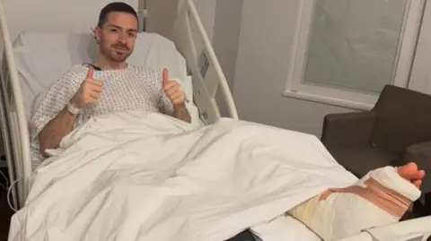 Midfielder Jack Grealish posing in a hospital bed with a bandaged foot