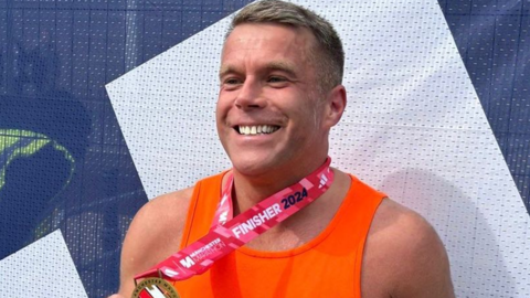 Stephen Melling wearing an orange vest running with a medal around his neck after finishing a run in Manchester