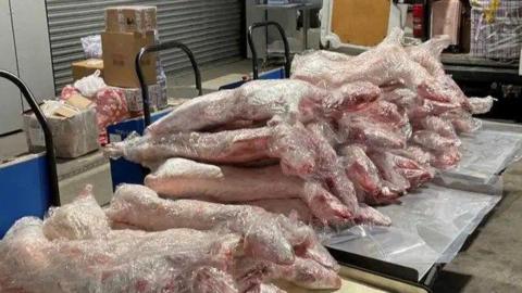 A pile of meat being inspected at the Port of Dover. It is piled up on a trollies, with other brown boxes in the background. 