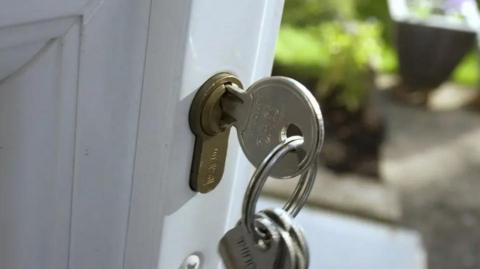 A close-up of a white door with silver key and gold lock.