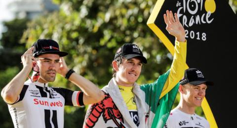 Geraint Thomas with a Welsh flag waves on the podium of the 2018 Tour de France