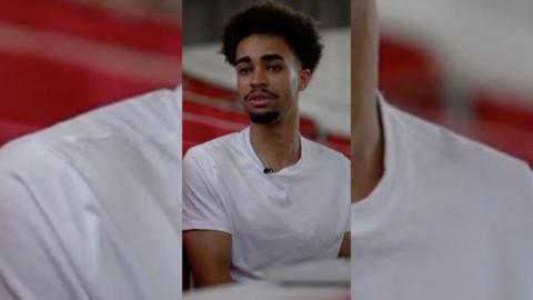Young man with short dark hair wearing a white t-shirt.