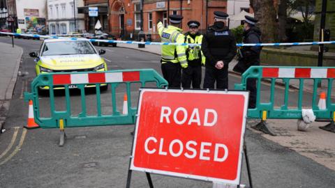 A group of police officers standing behind a road closed sign