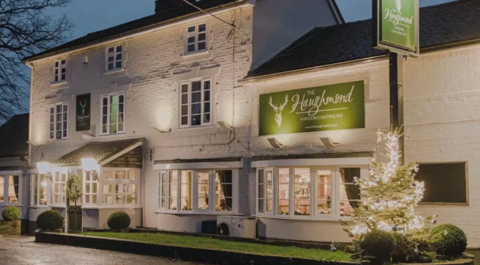 A large white building with a brown tiled roof and large bay windows and two green signs which both read The Haughmond