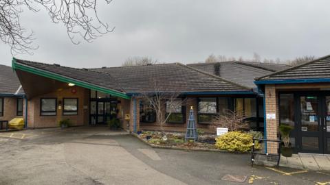 A single-story building with a small bed of plants outside the front entrance.