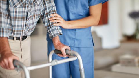 Cropped shot of a woman assisting her elderly patient with a walker for support