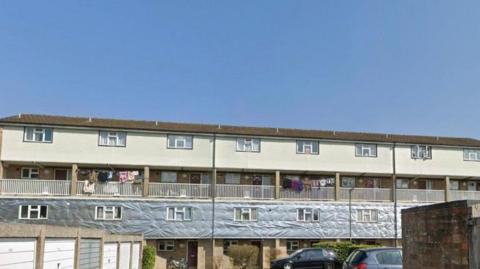 The exterior of a long block of flats in Woking, with cream coloured cladding around its modern windows and brown tiles on its rooves.