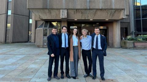 Four men and a woman stand outside Liverpool Crown court, their arms round each others' shoulders.