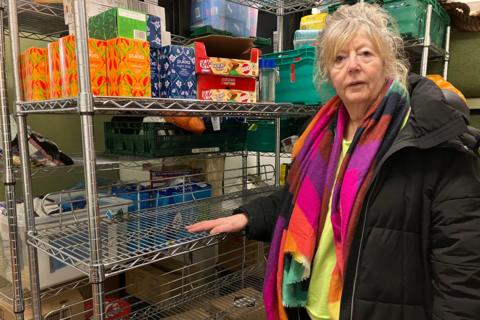 Fiona Nicol stood in front of part empty shelves. She is wearing a colourful scarf and black coat.