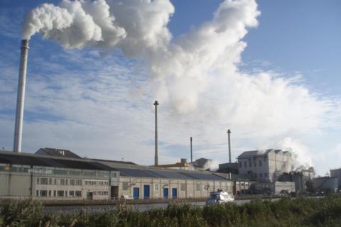 A factory with clouds of steam rising into the air on a sunny day.