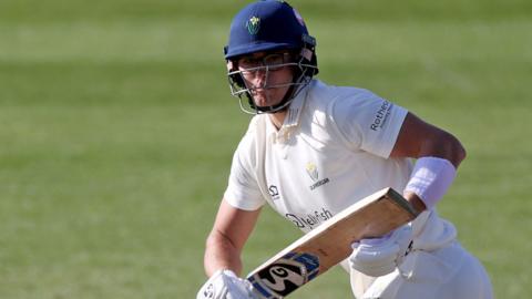 Asa Tribe wearing batters helmet holds bat