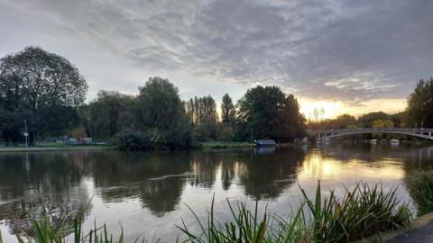 The River Thames with a bridge over it sits almost empty aside from one boat in the distance under a low sun and dark grey clouds