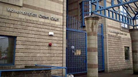 The outside of Wolverhampton Crown Court, with silver lettering on the front of the building and blue metal gates at the entrance.