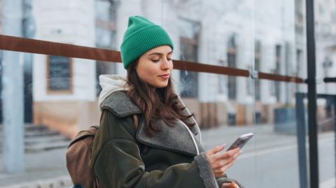 Young woman at bus stop looks at her phone