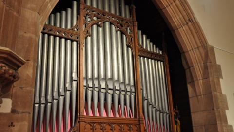The front of the pipe organ whcih is set in a stone archway in the cathedral. It has large metal pipes standing upright held in place by ornate woodwork. 