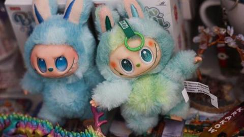 Labubu toys are seen in a shop. They have blue and green fur, large eyes and upright ears, which are part of their "monster elf" design.