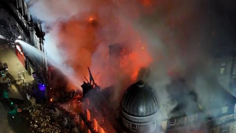Aerial view of Forsyth building ablaze, covered in smoke with water being sprayed from a fire engine
