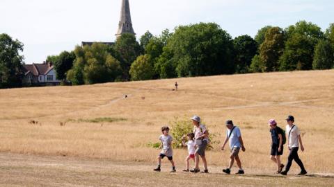 A group of people walk in Brockwell Park, south-west London, with the grass scorched