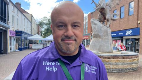 Nick Barber in Taunton town centre.  He is standing on a pedestrianised street with shops either side.