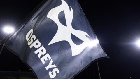 Ospreys flag under floodlights during a night game