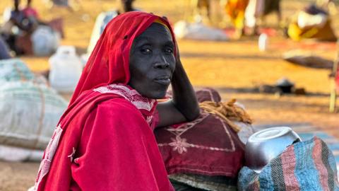 A woman wearing a red outfit and headscarf gazes past the camera