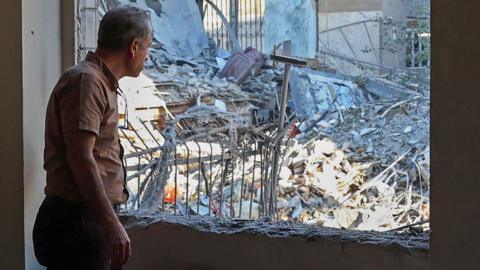 An Iranian resident looks out the window of his damaged home after Israeli-American strikes that according to local media reports destroyed the Rafi-Nia Synagogue and nearby residential buildings in Tehran, on April 7 2026.