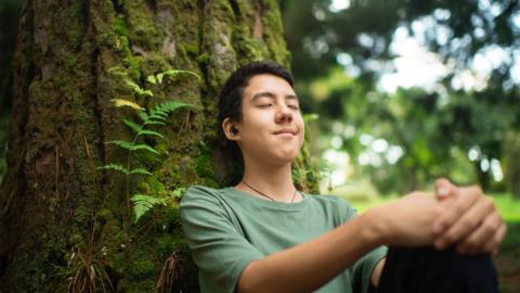 Teenage boy listening to music in a park in summer - stock photo