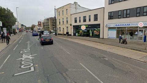 A Google Maps screengrab showing London Road in Gloucestershire. The image shows a high-street with a restaurant and a pharmacy on the right side.