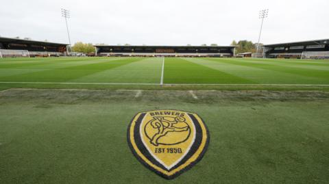 A view of the inside of Burton Albion's Pirelli Stadium with the club emblem beside the pitch